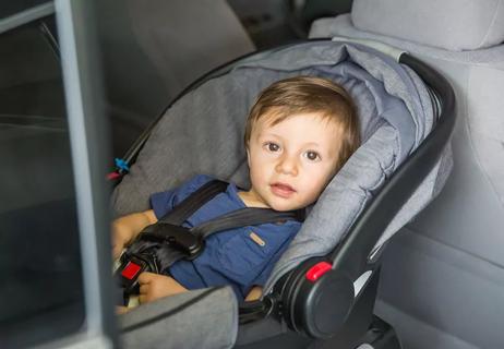 Older child belted into rear-facing care seat which is in the back sear of the car.