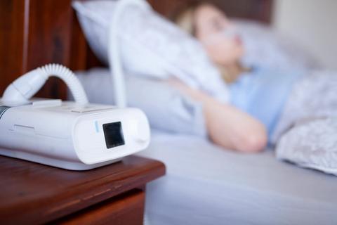 CPAP machine on night stand, as person sleeps with the CPAP mask on