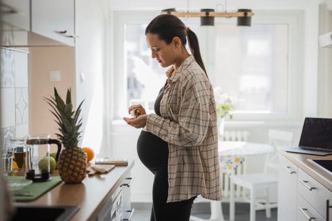 Pregnant woman standing in kitchen, pouring medication into hand