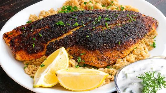 Blackened salmon on brown rice white plate, with a cucumber sauce in separate bowl