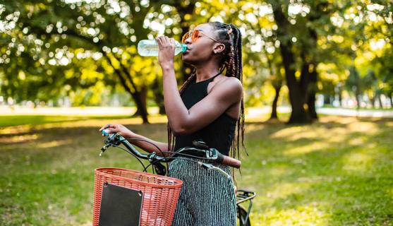 Person standing next to bike, drinking a bottle of water