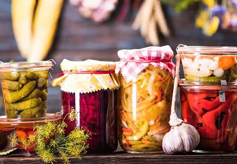 Homemade canning of assorted vegetables displayed on a natural wooden table.