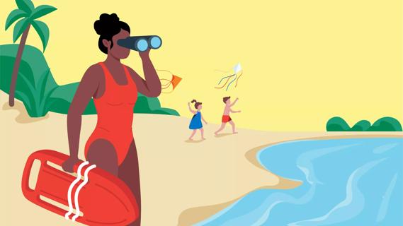 Lifeguard looking at water with binoculars while two kids fly kites on the beach