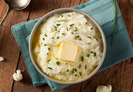 From above, a bowl of riced cauliflower with a melting pat of butter on top.