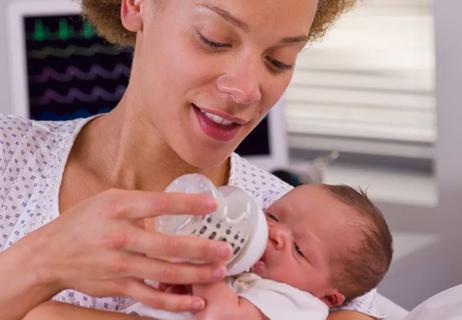 Parent holding newborn while feeding them formula.