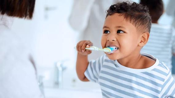 Parent helping toddler brush their teeth while in the bathroom
