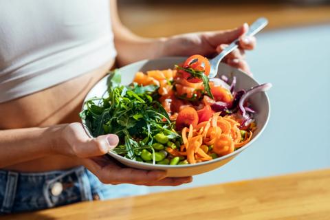 Person holding bowl of healthy salad, picking up a bite with a fork