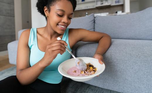 Smiling woman sitting on couch holding bowl of yogurt and granola