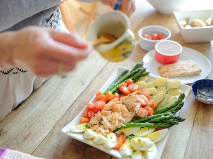 Person preparing healthy fish platter with veggies in kitchen