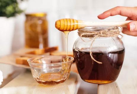 honey dripping from honey dipper which is resting on jar of honey