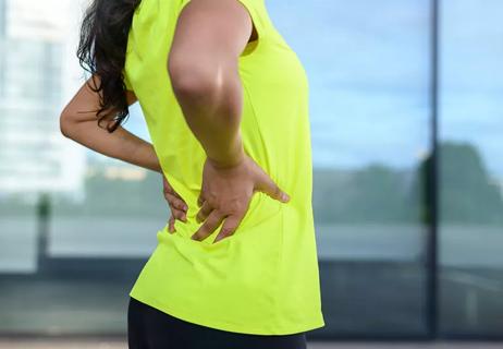 Woman in bright yellow running tank has both hand on her lower back as if in pain
