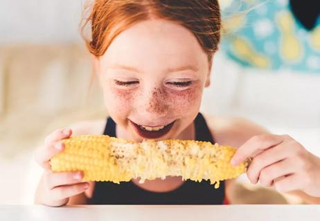 Young person with red hair enjoying eating corn on the cob with both hands.