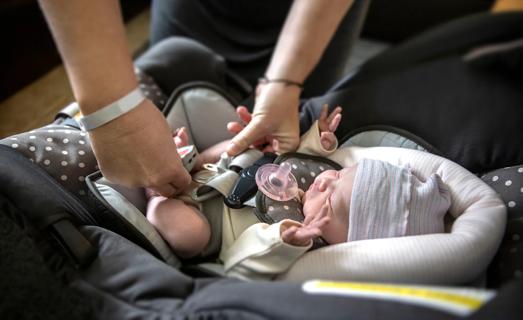 Hands buckling a newborn into a carseat