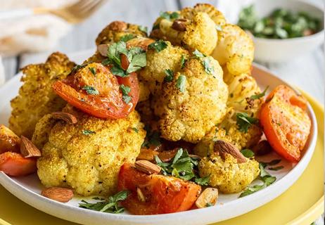 A plate holds a pile of crisp, roasted cauliflower, roasted tomatoes, almonds and cilantro.