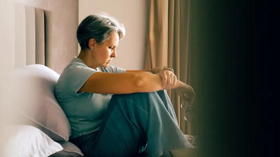 middle-aged woman looking down sadly while sitting on a bed