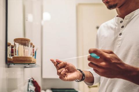 Person in bathroom, with jars of products on shelf, wrapping long piece of floss around fingers