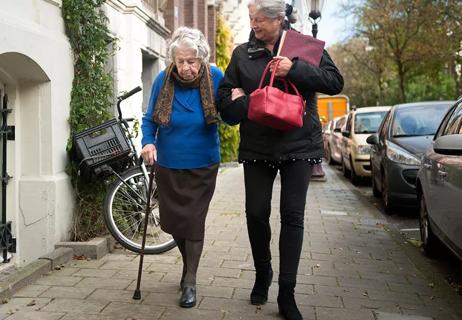 Elderly woman with cane gets assistance from friend on a walk