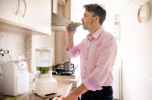 Person drinking smoothie in kitchen, with blender on counter