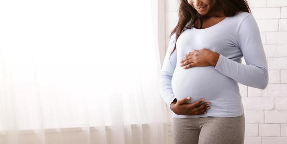 Afro woman enjoying her pregnancy, hugging her tummy