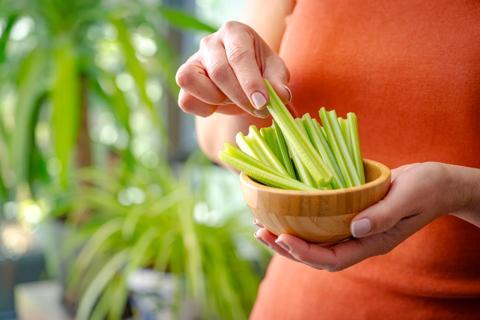 Person holding a wooden bowl of celery sticks