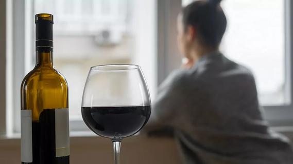 blurred person looking out window in background with glass of wine and bottle in foreground