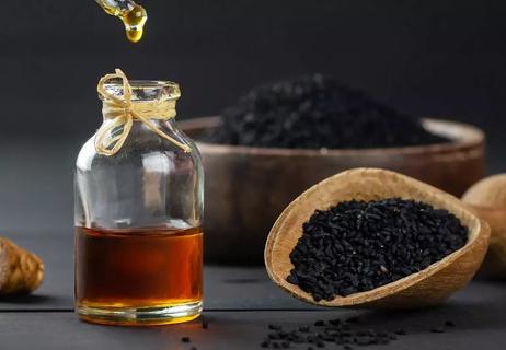 Black seed of cumin in a scoop on tabletop sitting by a vial of oil with dropper suspended above.