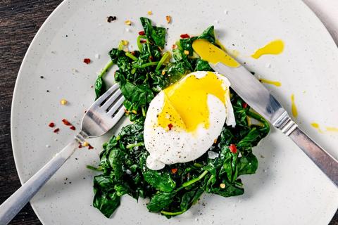 Poached egg on bed of spinach with red pepper, with fork and knife on plate