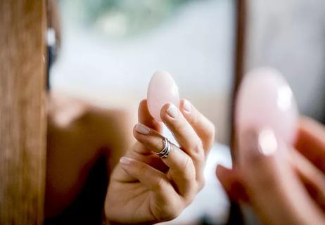A person holds up an egg-shaped quartz crystal, known as a yoni egg.