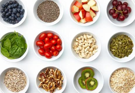 Bowls with apples, grapes, blueberries, tomatoes, kiwi, spinach, nuts and seeds