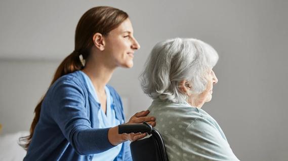 female caregiver with hand on back of elderly woman in wheelchair