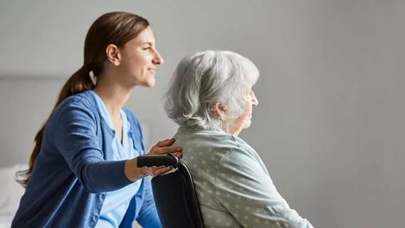 female caregiver with hand on back of elderly woman in wheelchair