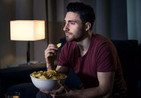 Person eats potato chips while watching television in a dark room