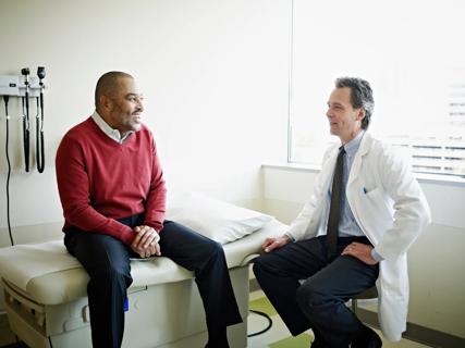 Smiling patient sitting on exam table, and healthcare provider sitting on stool, smiling and talking