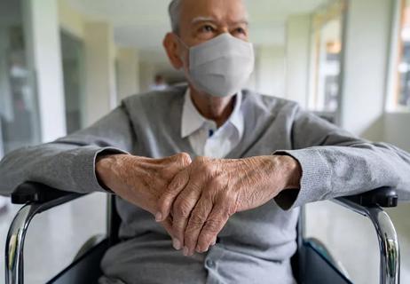 An older person sitting in a wheelchair wearing a mask