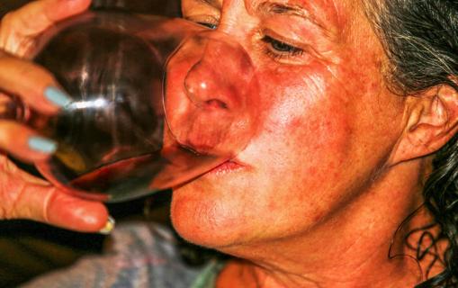 Person with a flushed face drinking a glass of wine