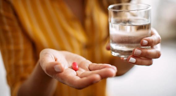 Hand holding red capsule, with other hand holding glass of water