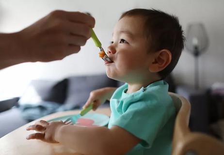 A person feeding a child who is sitting in a high chair