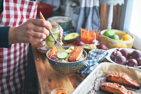 Person preparing a bowl with salmon and avocado and other vegetables