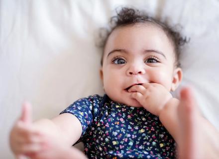 Happy baby lying on back with hand in their mouth