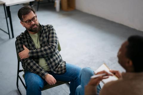 Person sitting in chair across from therapist/counselor in a chair with notepad