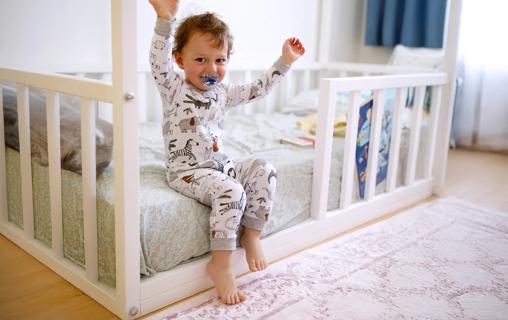 Happy toddler in pjs sitting on edge of their toddler bed