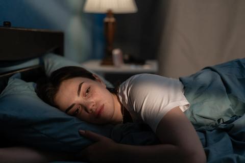 Person lying in bed on their side at night with their eyes open