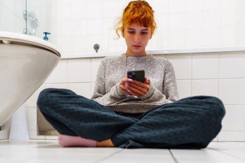 teen sitting in bathroom with phone