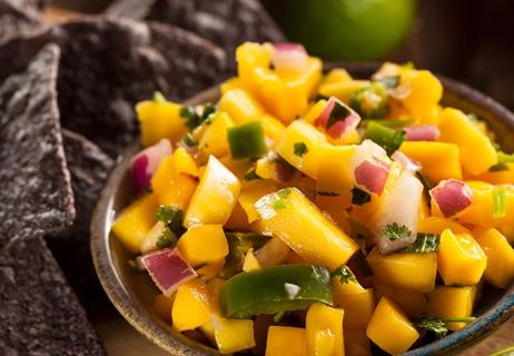 Mango salsa in small wooden bowl with chips in background.