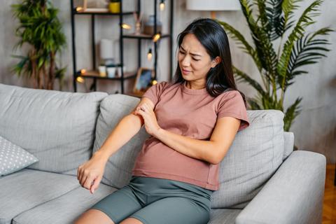 Pregnant woman sitting on couch, scratching her arm
