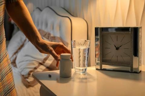 Person setting down a bottle of sleep medication on their nightstand, next to glass of water and clock