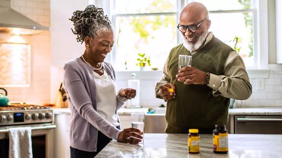 Older couple standing in kitchen taking vitamins