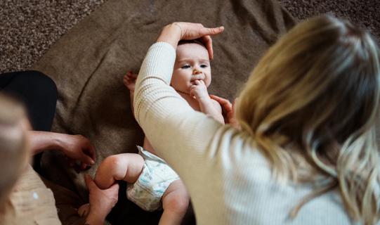 Female gently stretching a baby’s head and holding their shoulder in place on a blanket