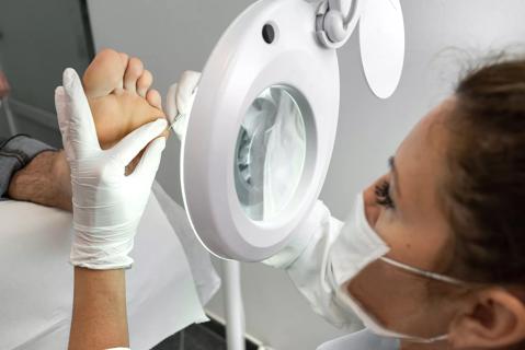 Medical technician looking through large, lighted magnifying glass, working on patient's foot