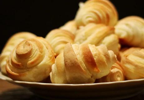A closeup of crescent rolls in a brown bowl on a dark background.